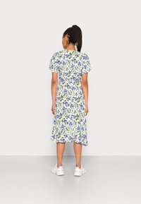 Robe florale avec des manches courtes, fond blanc, et fleurs bleues avec des feuilles vertes. Ourlet évasé au-dessus des genoux, associée à des baskets blanches.