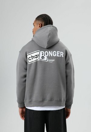 Grijze hoodie met losse pasvorm, met gedurfde witte tekst op de achterkant. Zachte textuur en geribbelde boorden maken het ontwerp compleet.