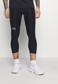 Sorte sportsleggings med tætsiddende pasform, der har et hvidt Under Armour-logo på forsiden og en glat, strækbar tekstur.