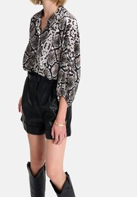 Blusa con stampa serpente in tonalità di nero e beige, con una vestibilità ampia e maniche arricciate, abbinata a pantaloni corti in pelle nera a vita alta.