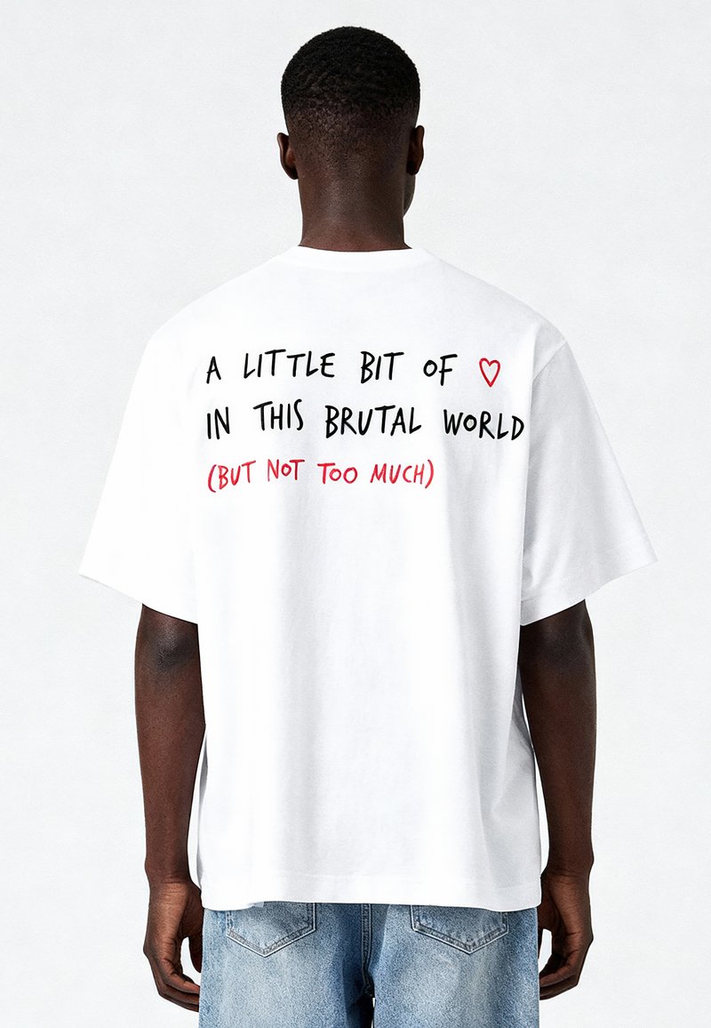 Balts pārāk liels T-krekls ar melnu un sarkanu tekstu aizmugurē: "MAZLIET ♥ ŠAJĀ BRUTĀLAJĀ PASAULĒ (BET NE PĀRSPĒJOT)."