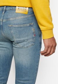 Lichtblauwe denim jeans met een slim fit, met een gouden label met "Scotch & Soda" en meerkleurige stiksels op de achterzak.