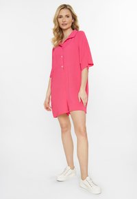 Puffärgad, kortärmad rompers i kläddesign med krage, avslappnad passform och sidofickor, tillsammans med vita sneakers.