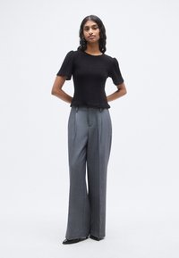 Μαύρο τοπ με υφή, κοντά φουσκωτά μανίκια και λαιμόκοψη με κυματιστό σχέδιο, συνδυασμένο με γκρι, ψηλόμεσα, φαρδιά παντελόνια και μαύρα μυτερά παπούτσια.