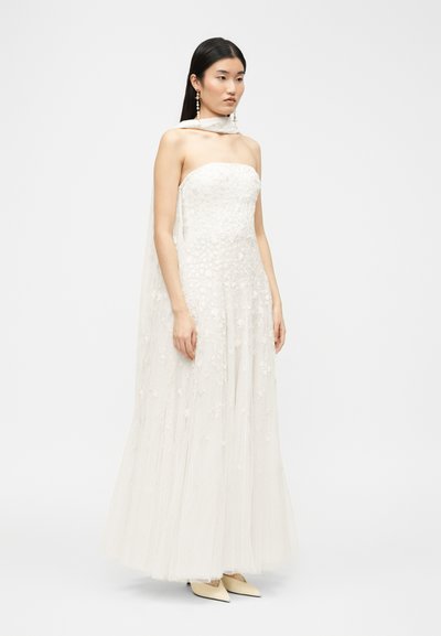 Naine kannab õlgadeta valget lillelist pitsist õhtukleiti, mille ümber on pikk õhuline sall kaela ümber drapeeritud ning tal on kõrvarõngad, millest ripuvad pärlid.