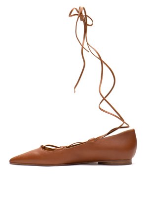 Brauner flacher Lederschuh mit spitzer Zehenpartie, langen Wickelriemen um den Knöchel und niedrigem Blockabsatz, vor weißem Hintergrund dargestellt.