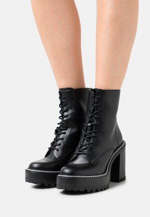 Schwarze Lederstiefeletten mit einer klobigen Plateausohle, ausgestattet mit einer Schnürung auf der Vorderseite, kontrastierenden Nähten und einer strukturierten Gummisohle.