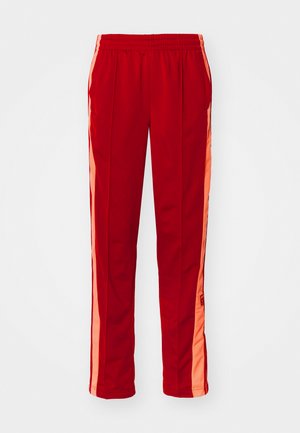 Sarkanas sporta bikses ar elastīgu jostu, divām sānu kabatām un kontrastējošām oranžām sānu svītrām. Gluda, viegla auduma.