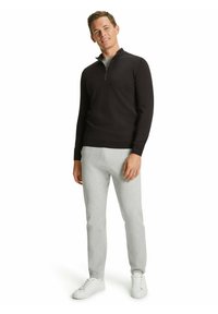 Felpa nera con zip, t-shirt grigia sotto, pantaloni di tuta grigi chiari, sneaker bianche. Design semplice, texture liscia, vestibilità casual.