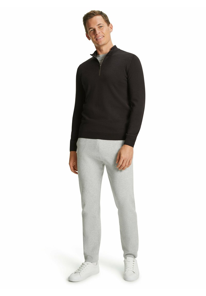 Felpa nera con zip, t-shirt grigia sotto, pantaloni di tuta grigi chiari, sneaker bianche. Design semplice, texture liscia, vestibilità casual.