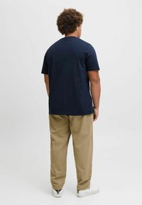 Marineblå bomulds t-shirt med korte ærmer, parret med beige bukser. Modellen bærer hvide sneakers med lynlåsdetaljer ved anklen.