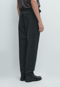 Schwarze, locker sitzende Hosen mit elastischem Bund, Seitentaschen, aus strukturiertem Stoff, kombiniert mit schwarzen Leder-Stiefeletten.