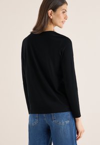 Mustat pitkähihaiset paidat, joissa on pyöreä kaula-aukko, on valmistettu pehmeästä kankaasta. Yhdistetty vaaleansinisiin farkkuihin. Minimalistinen muotoilu, ei näkyviä kuvioita.