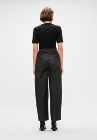 Jeans pretos de cintura alta com um corte largo, dois bolsos traseiros e detalhes de costura visíveis. Combinados com uma blusa justa preta canelada e botas de tornozelo.