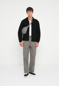 Gray crossbody bag, black collared shirt, white t-shirt, gray checkered pants, black sneakers. Plain background, front view of model.