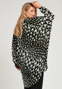 Camisa larga de estampado en blanco y negro con un corte holgado, que presenta un dobladillo redondeado, botones en los puños y una tela ligera con una textura suave.