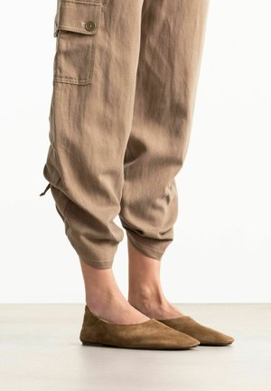 Bruine suède platte schoenen met spitse neus, gedragen bij beige cropped broeken met een knoopsluiting aan het zijzakje en elastische boorden.