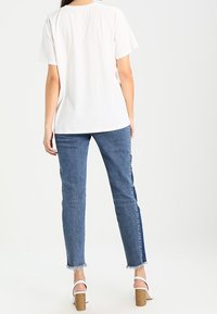 Valkoinen lyhythihainen T-paita yhdistettynä sinisiin korkeavyötäröisiin farkkuihin, joissa on rispaantunut helma ja kontrastivärinen sivupaneeli, päällä valkoiset korkokengät.