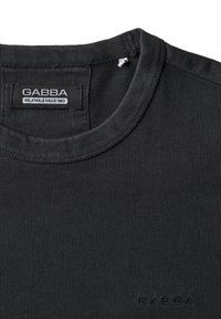 Sort bomulds t-shirt med rund hals, der har et synligt mærke med teksten "GABBA" og diskrete stikninger ved halsen.