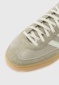 Grüner Wildledersneaker mit weißen Schnürsenkeln und seitlichen Streifen, ausgestattet mit einer Gummisohle und strukturierten Oberflächen.