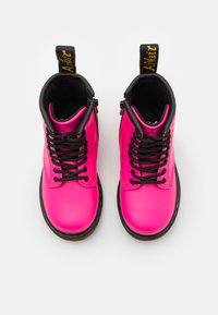 Botines de cuero rosa con cordones y forro negro. Presentan una etiqueta de logo amarilla en el talón y una suela de goma negra redonda.