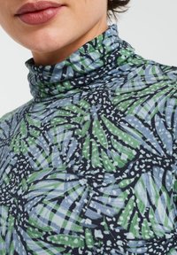 Halskrage toppen med ett blått och grönt bladmönster på en mörk bakgrund. Mjukt tyg med en åtsittande krage och intrikata tryckdetaljer.