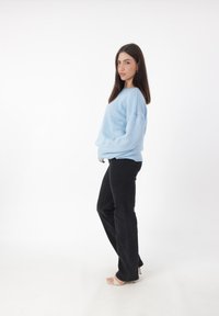 Jasnoniebieski, oversize sweter z teksturowanej tkaniny, połączony z czarnymi spodniami prostymi i beżowymi sandałami na obcasie.