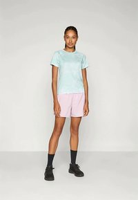 Heledsinine tie-dye t-särk, lühikesed varrukad; roosad lühikesed püksid, elastne vöökoht; mustad kingad ja sokid. Mudel seisab käed külgede peal.