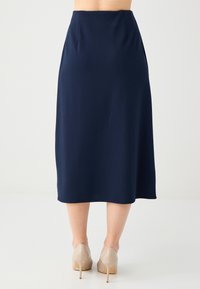 Gonna midi blu navy con una texture liscia, caratterizzata da una vita aderente e pieghe sottili. Abbinata a scarpe con tacco neutre.