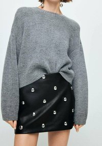 Suéter gris de punto con escote ancho, combinado con una falda de cuero sintético negra que presenta remaches plateados en un patrón.