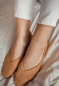 Bailarinas de ante en tono marrón con un corte en V profundo, combinadas con pantalones blancos hasta los tobillos y una delicada pulsera de oro en el tobillo.