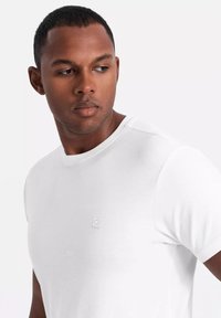 Biała koszulka z okrągłym dekoltem, wykonana z gładkiej bawełny, z subtelnym logo na klatce piersiowej. Krótkie rękawy i luźny krój.