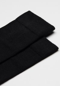 Schwarze Baumwoll-Beinwärmer mit weicher Textur, gerippten Bündchen und einem schlichten, ungeschmückten Design. Ideal zum Schichten bei kühlem Wetter.