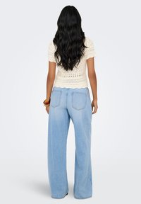 Jean large bleu clair à taille haute, avec des poches classiques et des passants de ceinture. Le haut assorti est un modèle tricoté de couleur crème.
