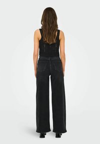 Jean large noir en denim, avec des poches arrière et une taille haute, associé à un crop top en dentelle noire.