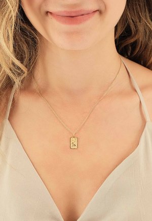 Collier en or avec un pendentif rectangulaire orné d'une illustration détaillée, suspendu à une chaîne fine. L'arrière-plan est de ton neutre.