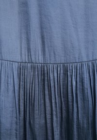 Blått tyg med samlade veck som skapar ett texturerat mönster och subtila vertikala veck över materialet.