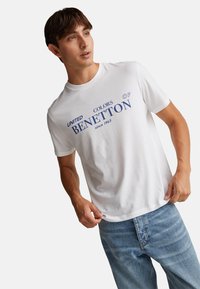 Bílý bavlněný tričko s modrým grafickým textem "UNITED COLORS OF BENETTON od 1965." Krátké rukávy a kulatý výstřih, mírně přiléhavý střih.