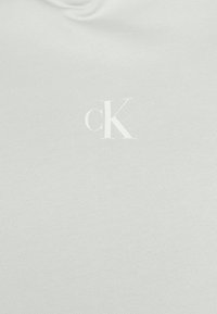 Tela blanca con un pequeño logotipo bordado en blanco "cK" centrado, que representa la marca Calvin Klein.