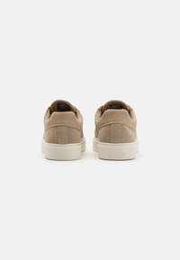 Beige suede sneakers with a low profile and white rubber sole. Features padded collar and embossed logo on the heel.