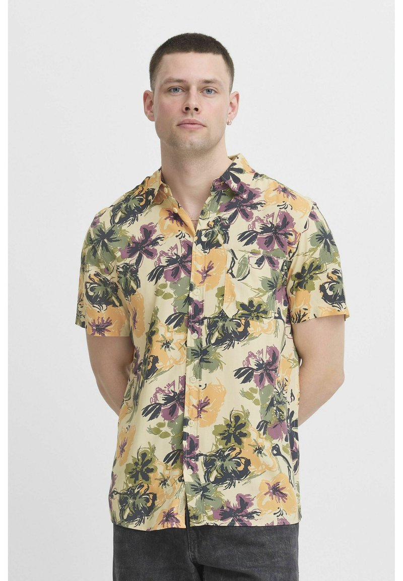 Korte mouwen shirt van een lichtgewicht, gele stof met een bloemenpatroon en groene, paarse en oranje accenten. Met knopen aan de voorkant en een zak.