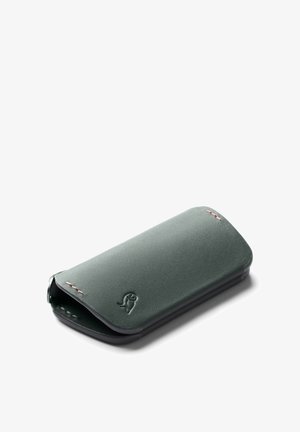 Étui de smartphone en cuir vert avec une texture lisse, des bords arrondis et une fermeture à rabat. Présente des coutures discrètes et un détail de logo.