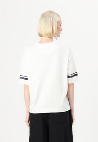Bílý bavlněný tričko s krátkým rukávem, s černými pruhy na rukávech. Volný střih a design s kulatým výstřihem.