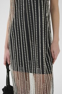 Rochie neagră cu un design din franjuri cu mărgele argintii și overlay din plasă. Prezintă linii verticale de mărgele și o siluetă ajustată. Include o geantă neagră.