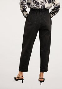 Svarta denimjeans med avslappnad passform, som har hög midja, två bakfickor och uppvikta anklar. Tillhållna med svarta klacksandaler.