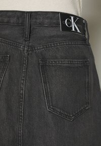 Jeans de denim negro con una etiqueta de Calvin Klein, que presentan un diseño clásico de cinco bolsillos y detalles de costura sutiles en la cinturilla y los bolsillos.