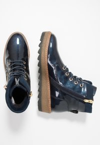 Stivaletti alla caviglia in pelle verniciata blu navy con suola in gomma testurizzata, dettagli in metallo dorato, design con lacci e cerniera laterale per un accesso facile.