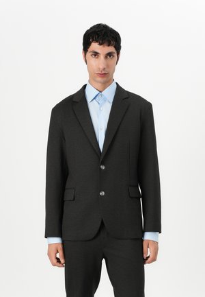Dark grey blazer with notched lapels, two front pockets, and two buttons. Paired with a light blue shirt featuring a spread collar.