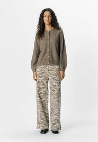 Cardigan marrón texturizado con escote redondo y cierre de botones, combinado con pantalones de corte ancho con estampado de cebra en tonos beiges y grises.