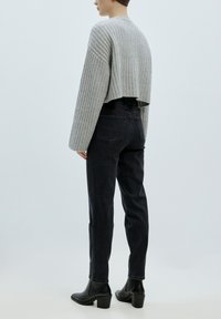 Grauer gerippter, verkürzter Pullover, schwarze hoch taillierte Jeans und schwarze Stiefeletten. Glatte Textur, lockere Passform und gerade Beinform.